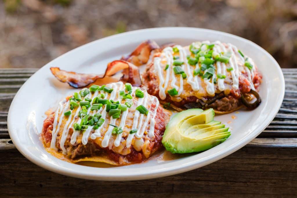 A plate of food topped with sauce and green onion and a side of avocado.