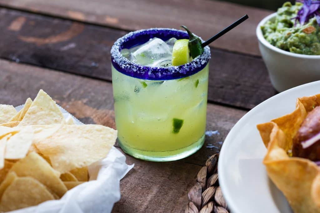A mixed drink surrounded by chips, dipping sauce, and an entrée.