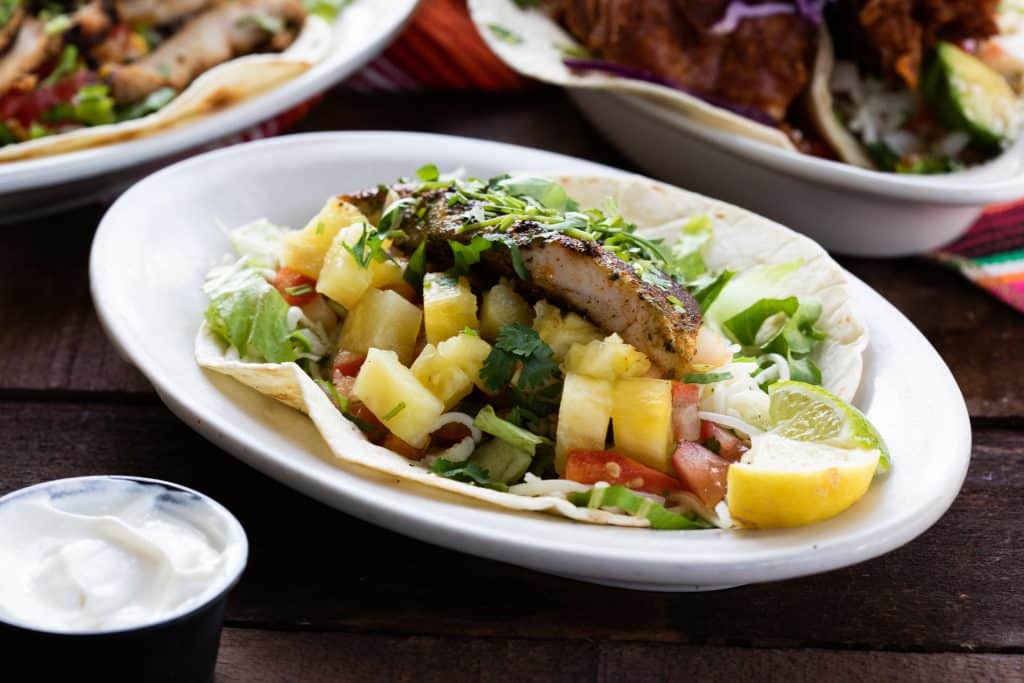 An entrée of fruits, vegetables, and seared meat on a tortilla.